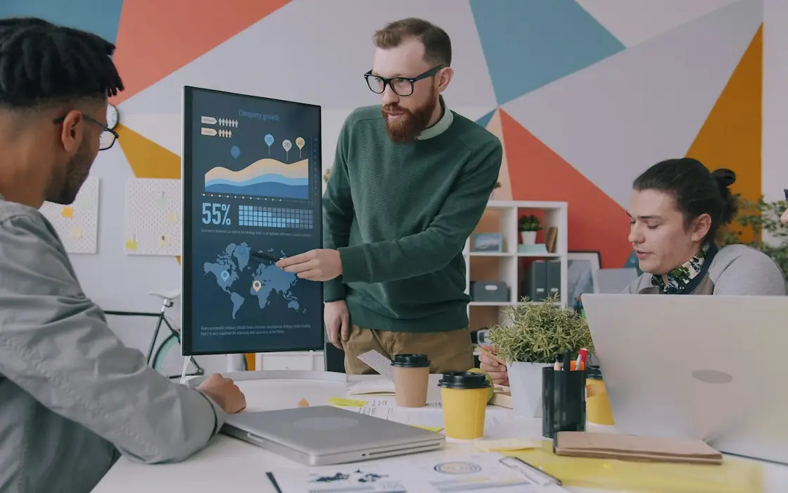 A team member pointing to charts on a large monitor while two colleagues follow along